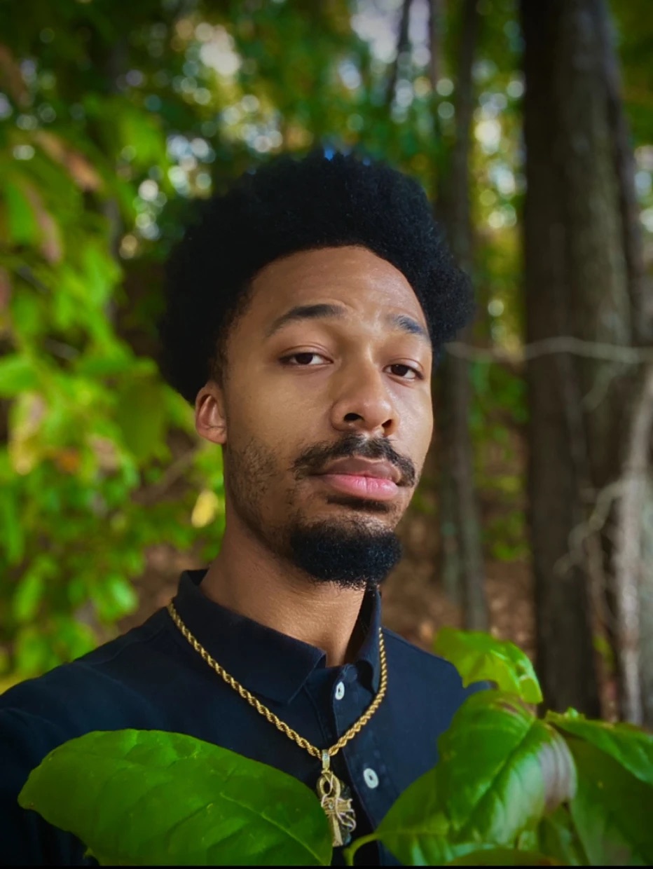 Jair standing calmly among green leaves in the woods
